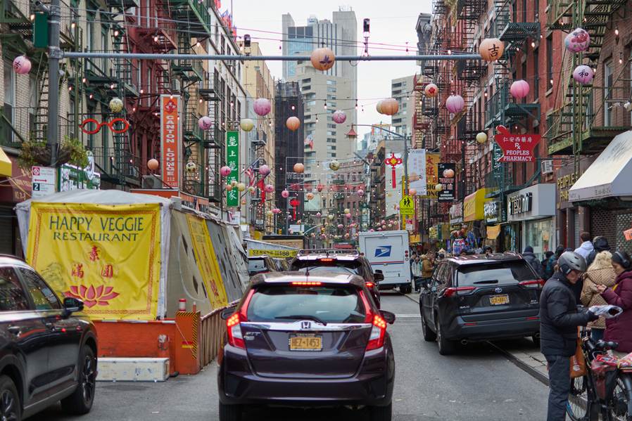 Busy city street with colorful hanging lanterns. "Happy Veggie Restaurant" is on a sign in the foreground.